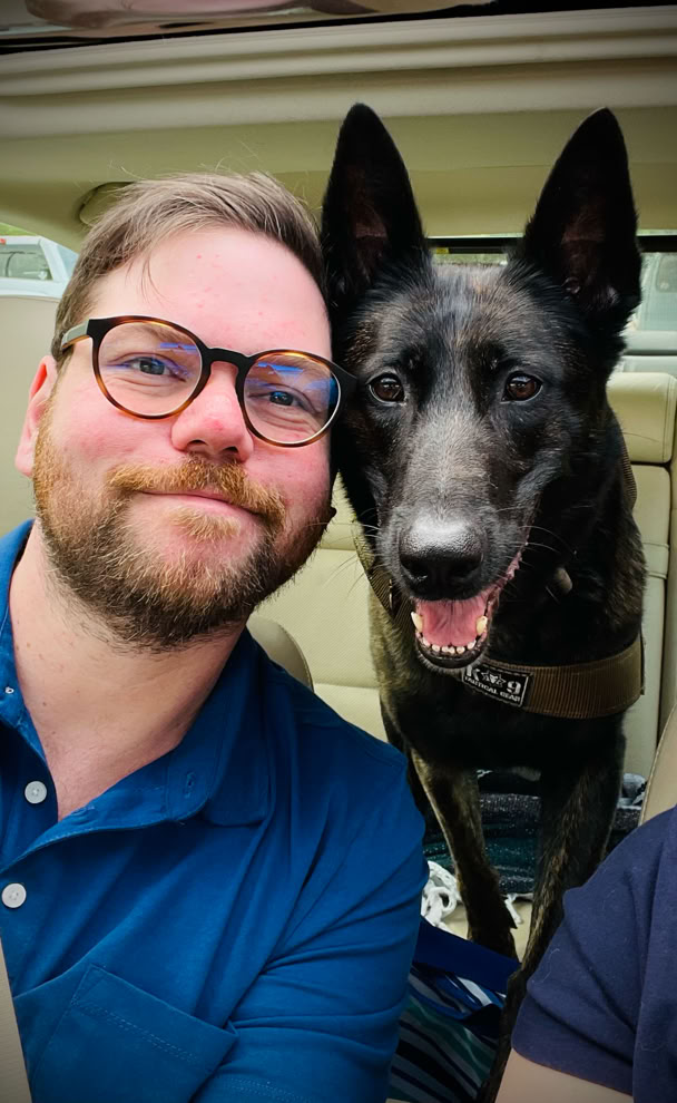 man with glass and beard in a blue shirt with dutch shepard malinois 